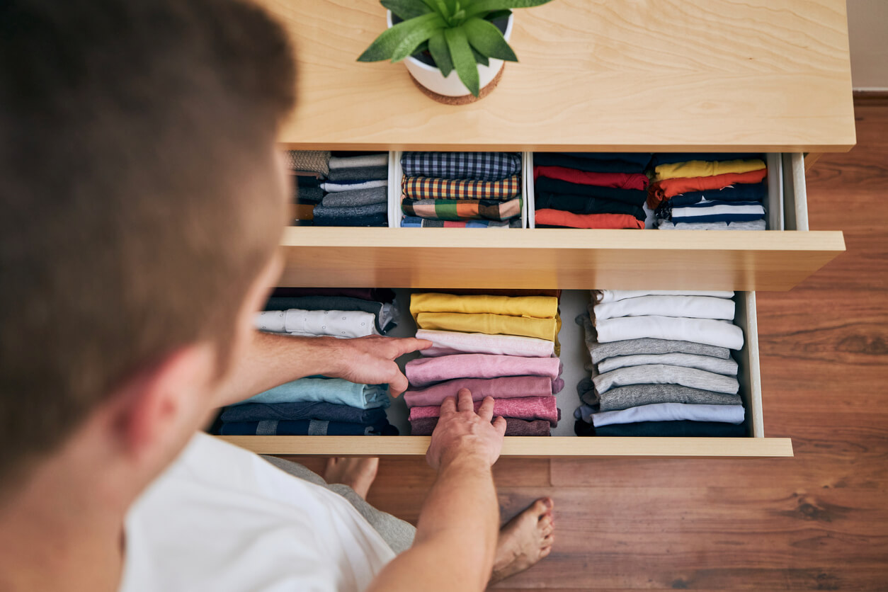 A man placing folded clothes in a dresser drawer.